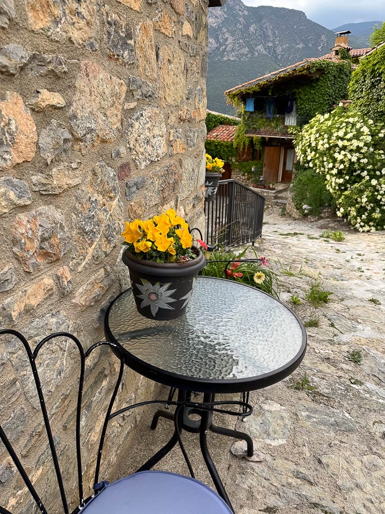 Taula amb dues cadires i un test amb flors a l'entrada de Cal Marinall